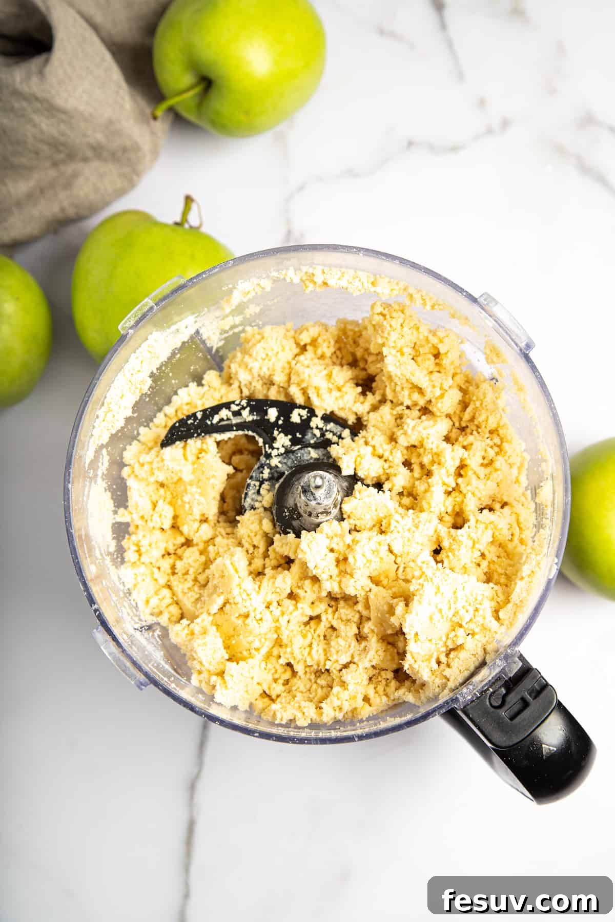 This classic yet easy and delicious Apple Pie recipe is made from scratch, with a buttery, flaky pie crust, fresh apple slices, pie spices, and brown sugar. Pie crust dough being prepared in a food processor, showing the flour and butter blending into coarse crumbs.