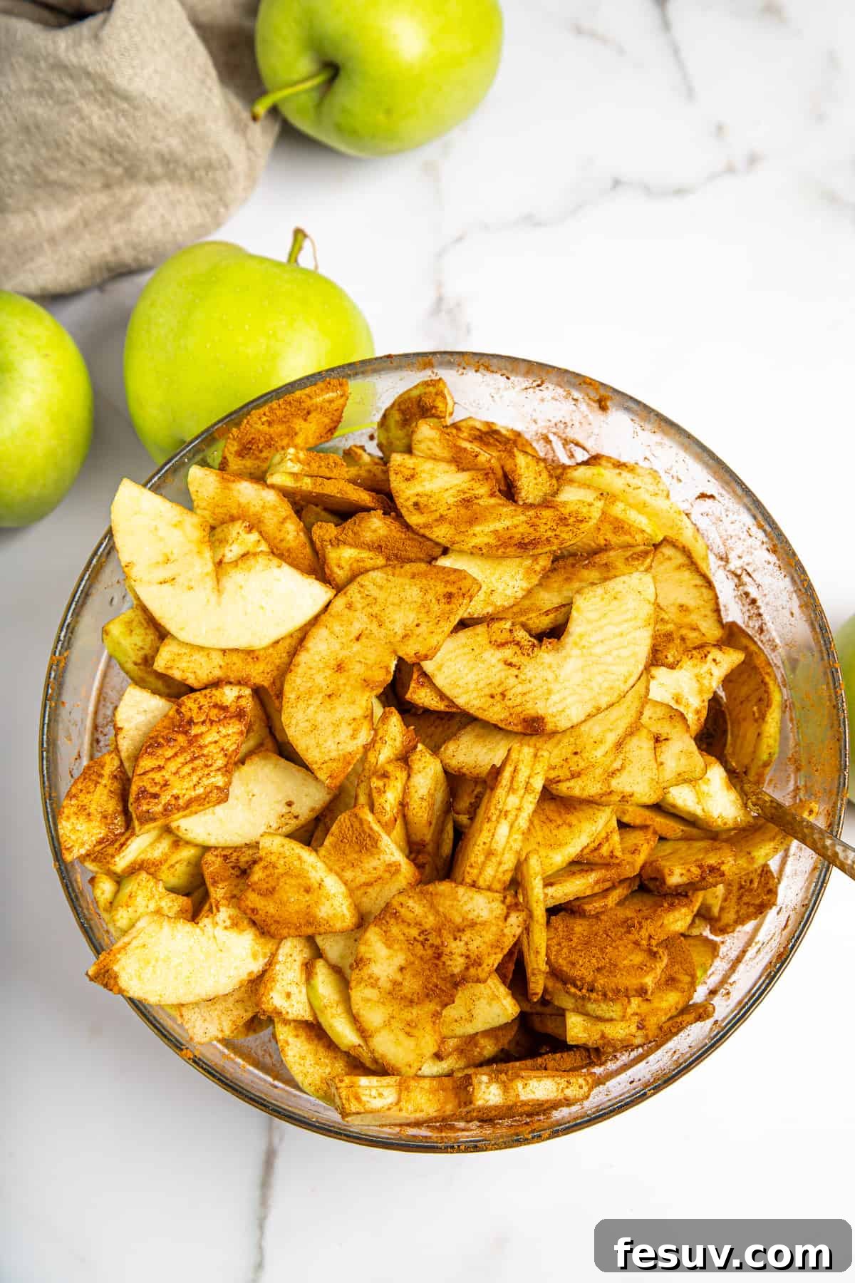 This classic yet easy and delicious Apple Pie recipe is made from scratch, with a buttery, flaky pie crust, fresh apple slices, pie spices, and brown sugar. Thinly sliced apples, coated evenly with a mixture of cornstarch, sugar, and spices, ready for the pie.