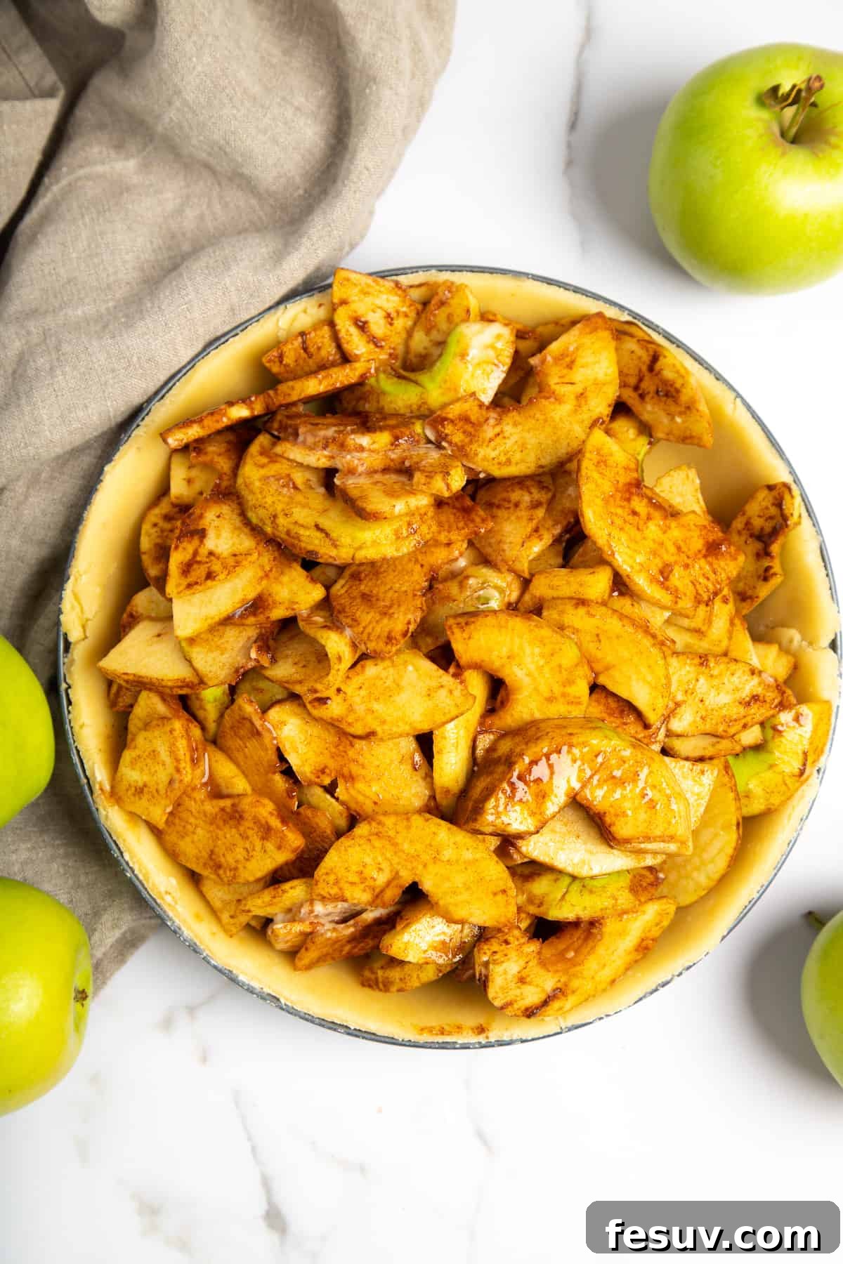 This classic yet easy and delicious Apple Pie recipe is made from scratch, with a buttery, flaky pie crust, fresh apple slices, pie spices, and brown sugar. Apple pie filling, consisting of spiced apple slices, neatly piled into an unbaked pie crust in a pie plate.
