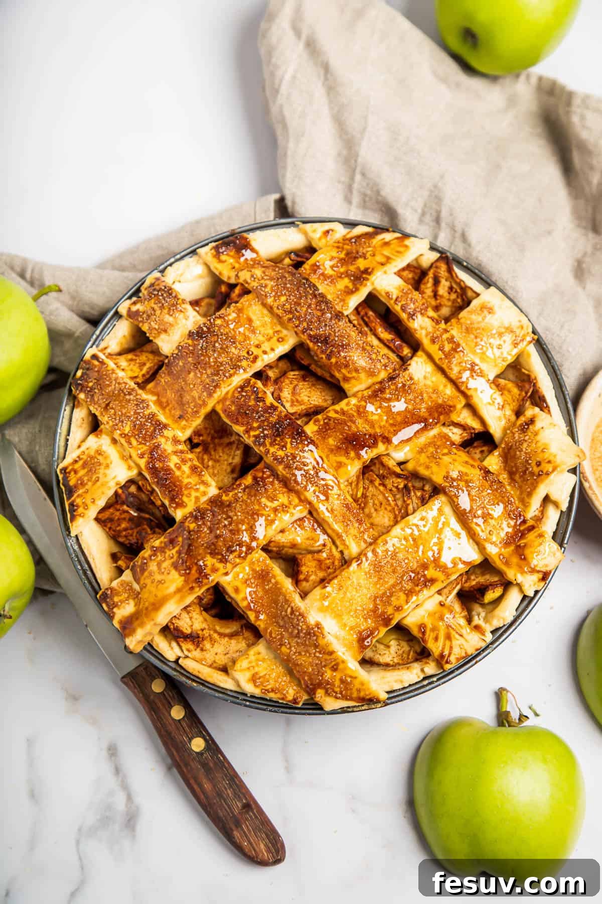 This classic yet easy and delicious Apple Pie recipe is made from scratch, with a buttery, flaky pie crust, fresh apple slices, pie spices, and brown sugar. A beautifully baked homemade apple pie with a golden, intricate lattice top, cooling on a wooden surface.