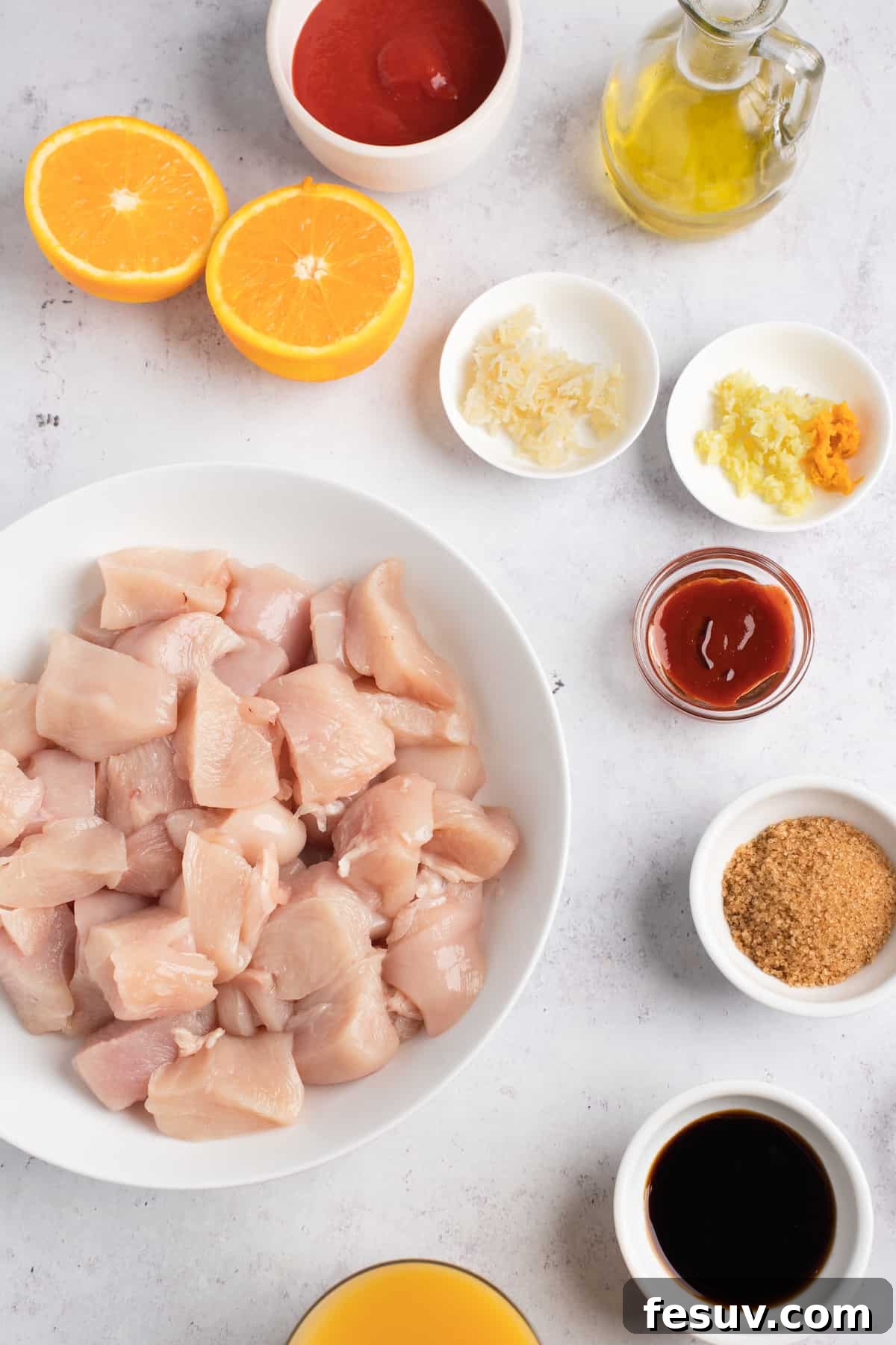 A collection of fresh ingredients for Instant Pot Orange Chicken: cubed chicken, tomato paste, oil, grated ginger, minced garlic, orange zest, sriracha, soy sauce, and orange juice.