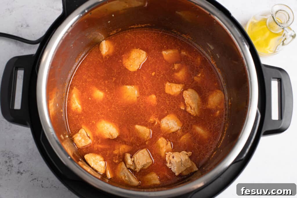Perfectly cooked chicken pieces coated in a rich, vibrant orange sauce inside the Instant Pot.