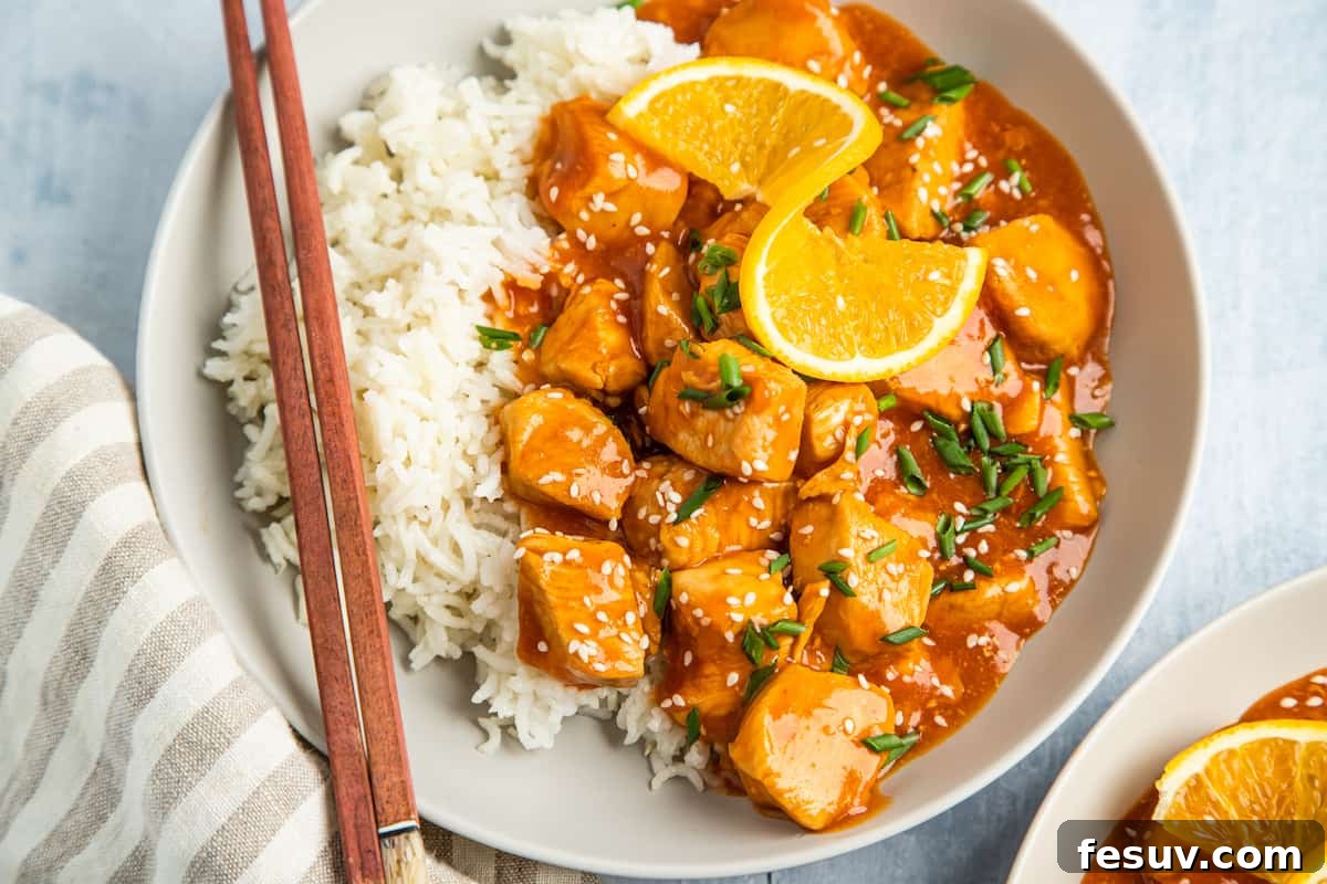 A single serving of orange chicken, artfully arranged on a plate with white rice and orange wedges, alongside chopsticks.