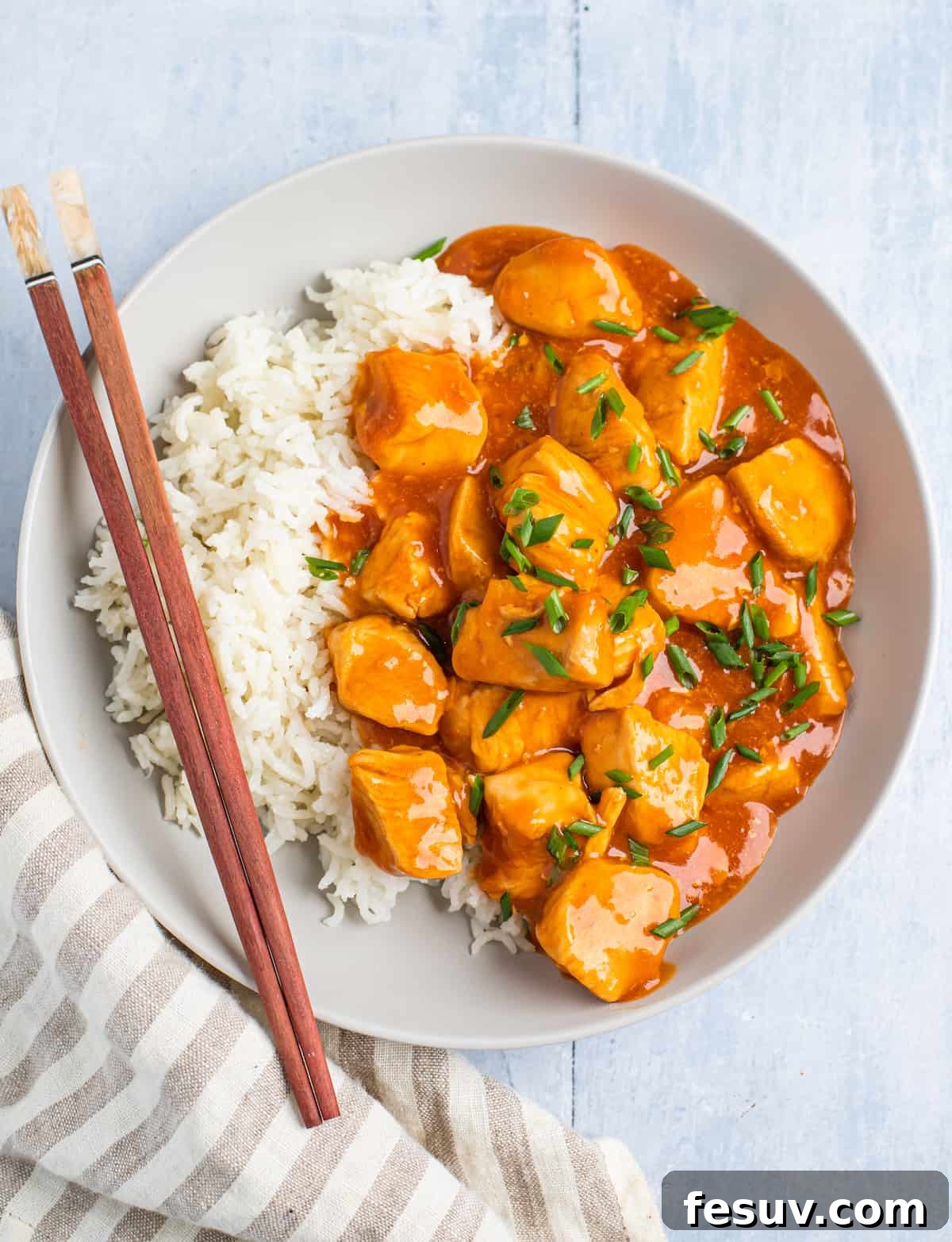 A perfectly centered overhead shot of a serving of orange chicken with white rice, garnished with green onions.