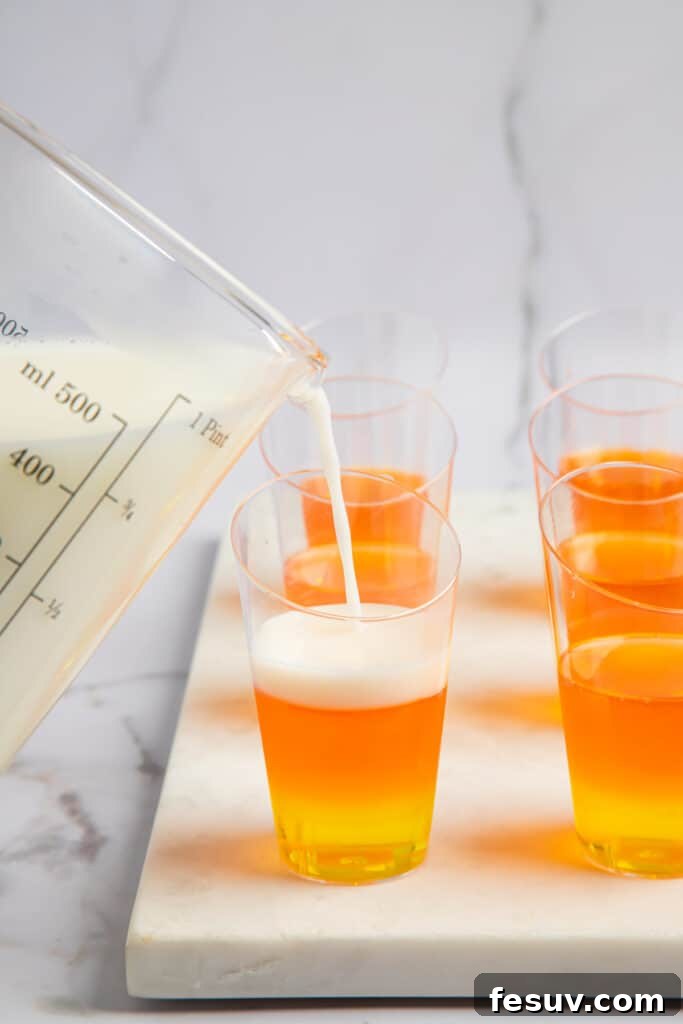 Vibrant Vodka Candy Corn Shooters 6 A creamy white layer being added to jello shot glasses on top of lemon and orange layers.