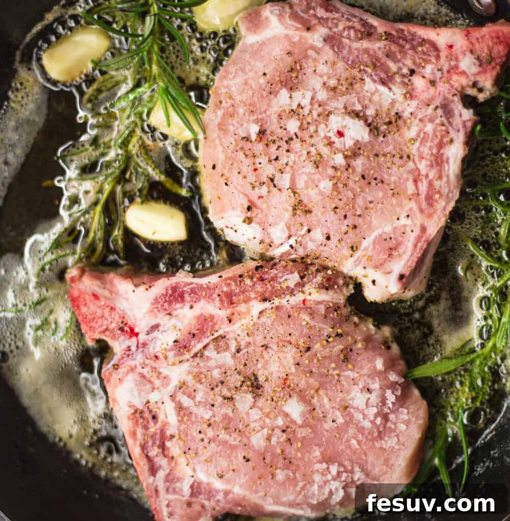 Searing thick-cut pork chops in a hot skillet with garlic cloves and sprigs of fresh rosemary, creating a flavorful crust.