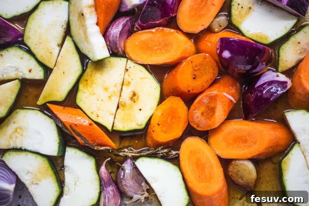 A mix of chopped root vegetables and sliced apples arranged in a roasting pan, ready to be cooked alongside the pork.