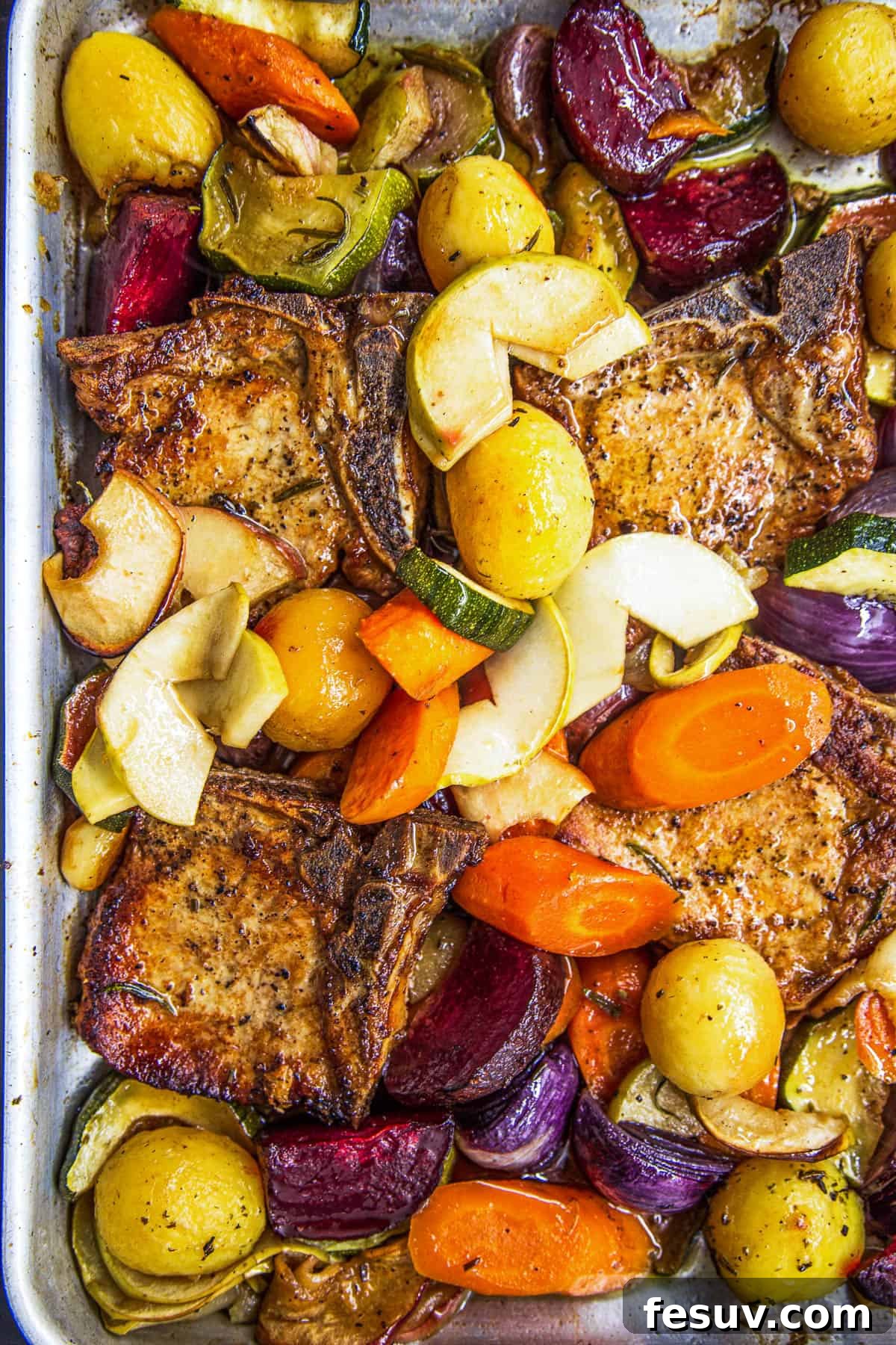 A close-up overhead view of the baking dish filled with perfectly cooked pork chops, caramelized apples, and tender winter vegetables, bathed in a rich apple juice and rosemary sauce.