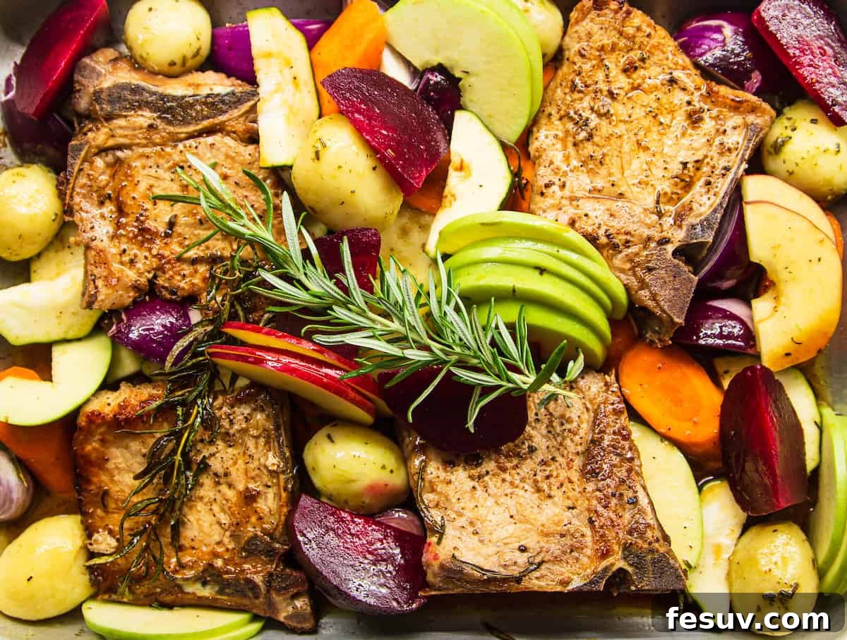 A high-angle shot of the baking dish, showcasing the juicy pork chops, golden-brown apples, and colorful roasted vegetables infused with apple juice and rosemary, ready to be served.