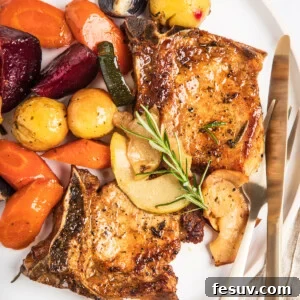 A plate of baked pork chops with apples and winter vegetables, garnished with a sprig of rosemary.