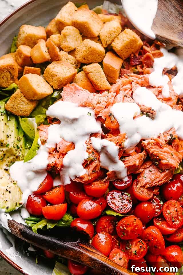 A close-up shot of Salmon BLT Salad, garnished with dressing and fresh herbs.
