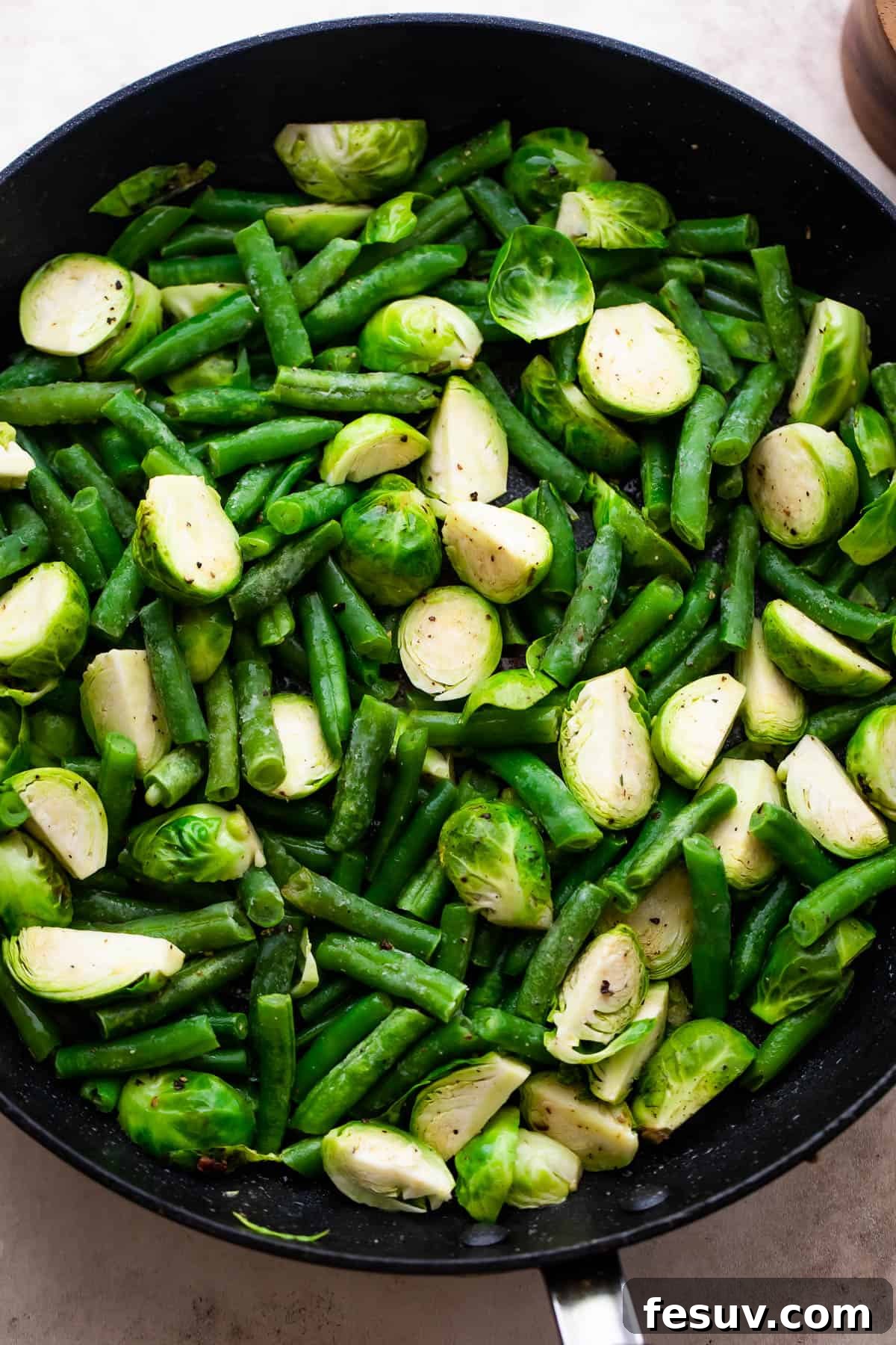 Sautéing Vegetables for Green Bean Casserole Fresh Brussels sprouts and thawed green beans gently sautéing in a black skillet, infused with savory bacon grease.