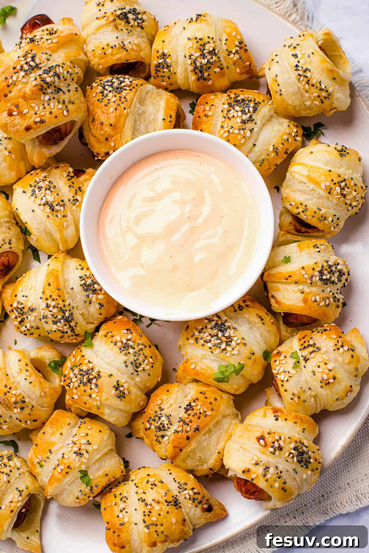 Super easy to make homemade Pigs in a Blanket are a delicious snack prepared with savory mini-sausages wrapped in golden, flaky puff pastry. A festive holiday platter brimming with an assortment of pigs in a blanket, artfully arranged around a central bowl of creamy dipping sauce, set against a backdrop of cozy, out-of-focus lights.