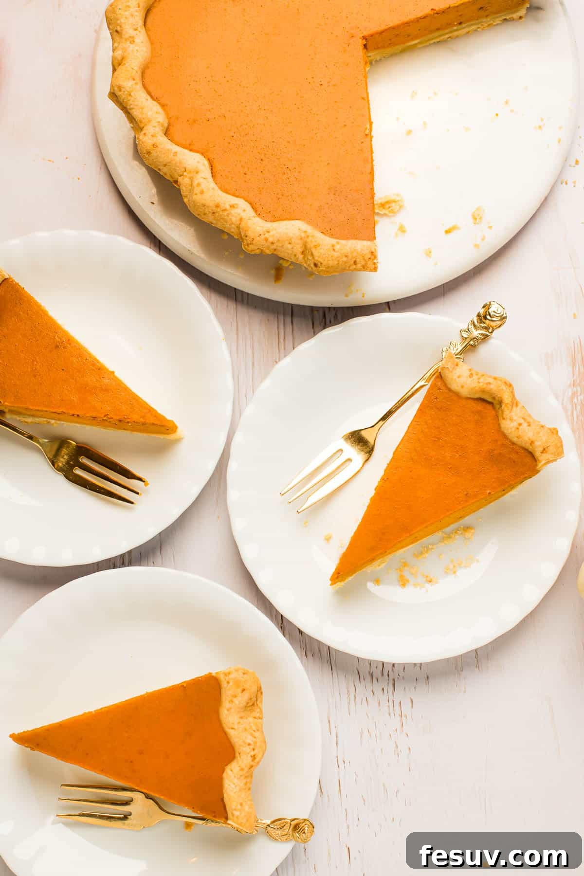 A beautifully baked pumpkin pie on a white serving platter, with one slice carefully cut and placed on a separate dessert plate, accompanied by a golden fork.