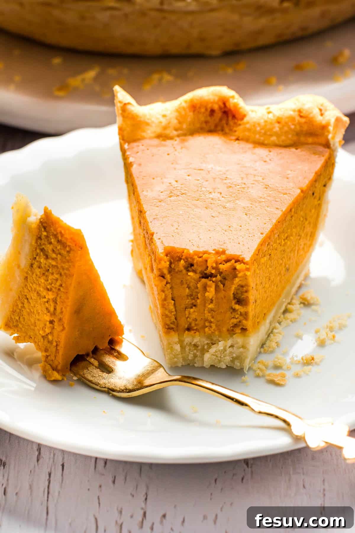 A perfect slice of pumpkin pie, rich and creamy, served on a pristine white plate with a fork ready for indulgence.