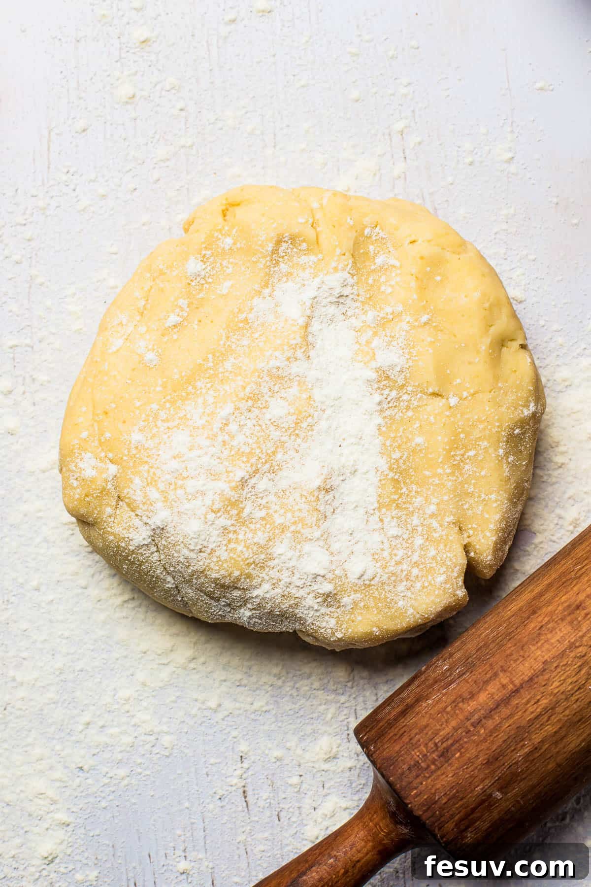 Freshly prepared pie dough on a floured surface, with a rolling pin resting nearby, ready to be shaped.
