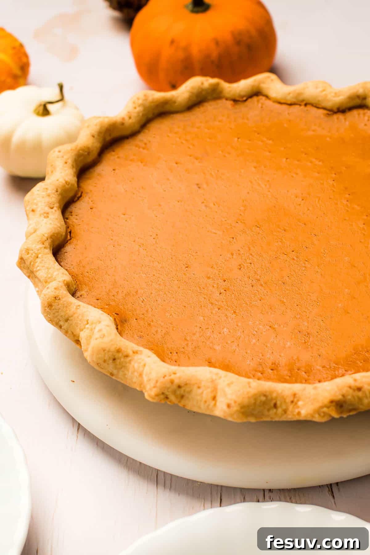 A perfectly baked pumpkin pie with a beautifully crimped crust, presented on a white serving plate, golden and inviting.