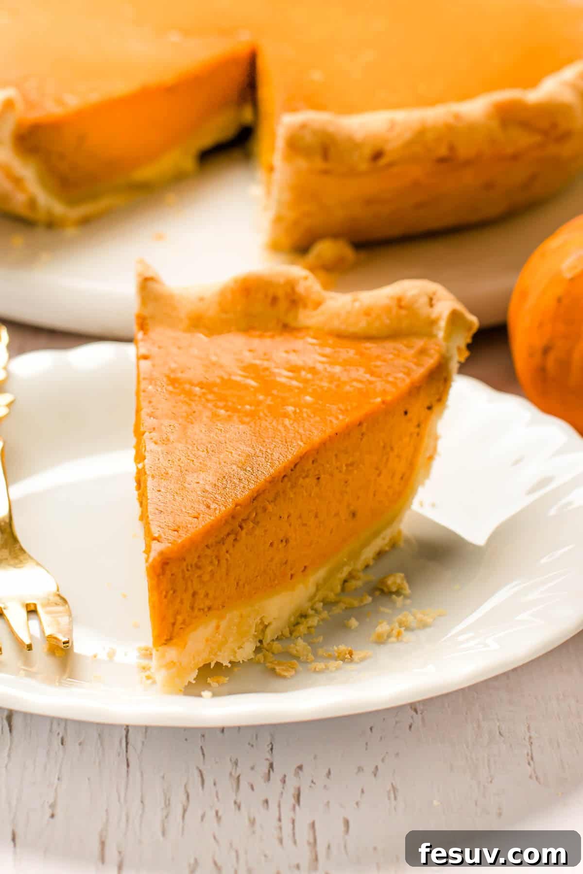 A delicious slice of pumpkin pie, perfectly cut and displayed on a white plate with a fork, inviting you to take a bite.