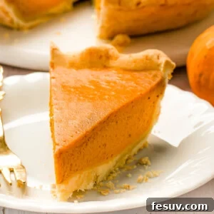 A pumpkin pie slice on a white plate with a fork.