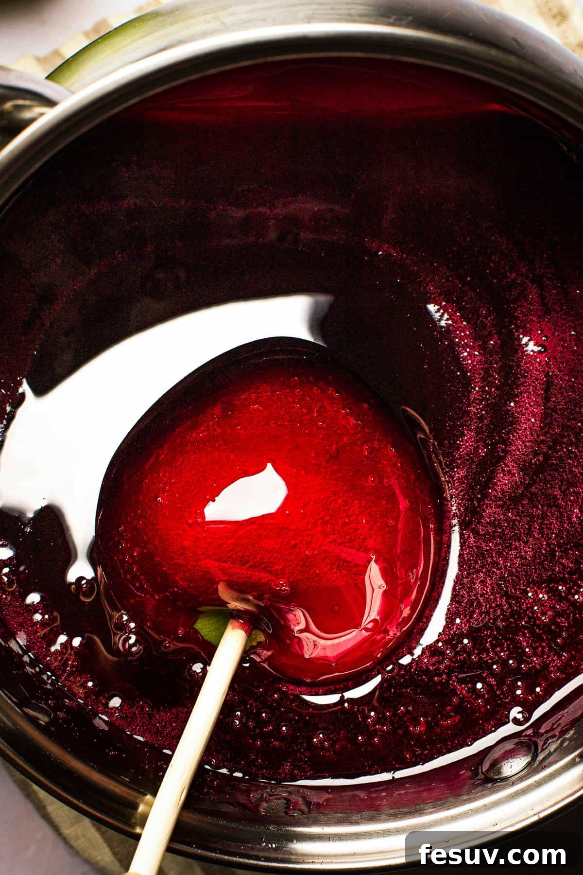 An apple, freshly coated in vibrant red candy, being carefully lifted from the saucepan of hot candy mixture, showcasing its glossy and flawless finish.