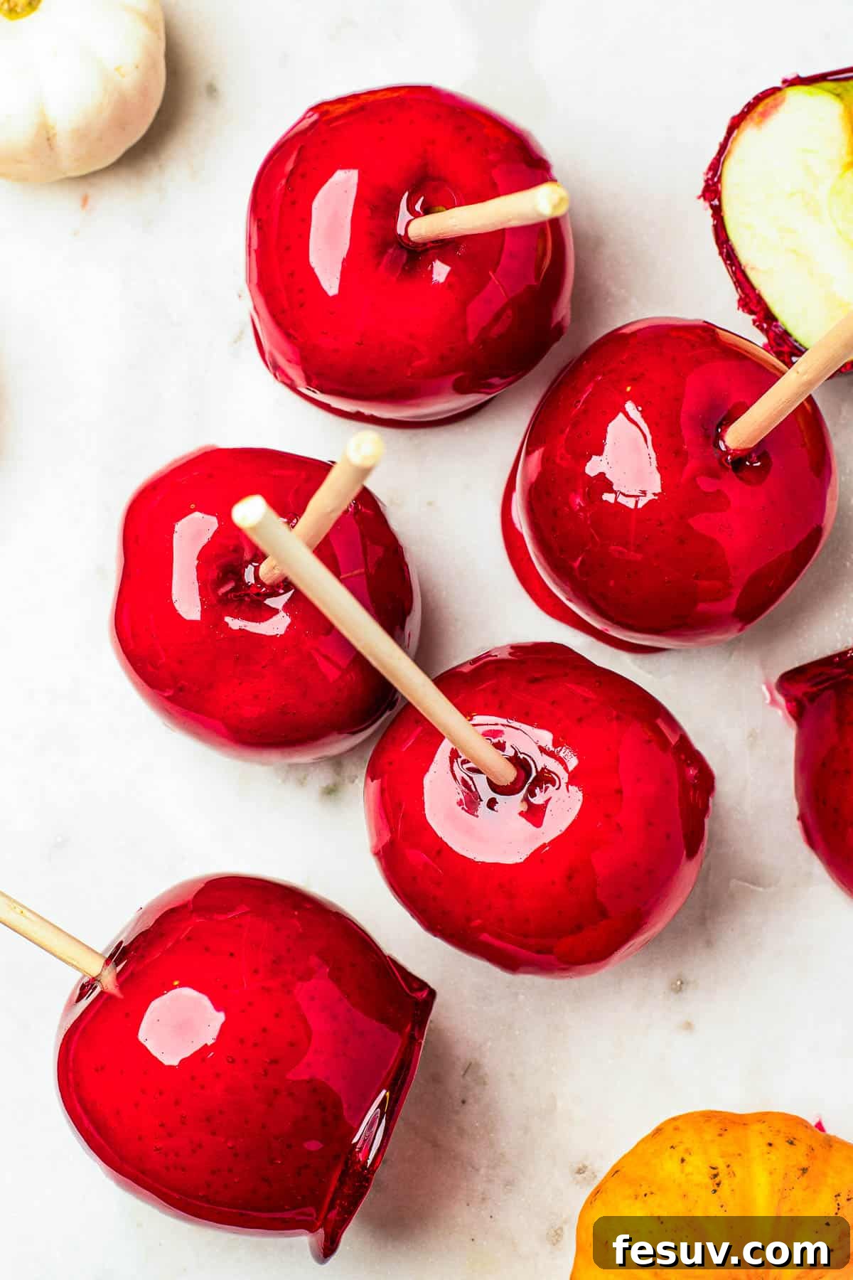 Several glistening ruby-red candy apples arranged elegantly on a white cutting board, with plain Granny Smith apples and an orange fringed placemat in the background, highlighting the transformation.