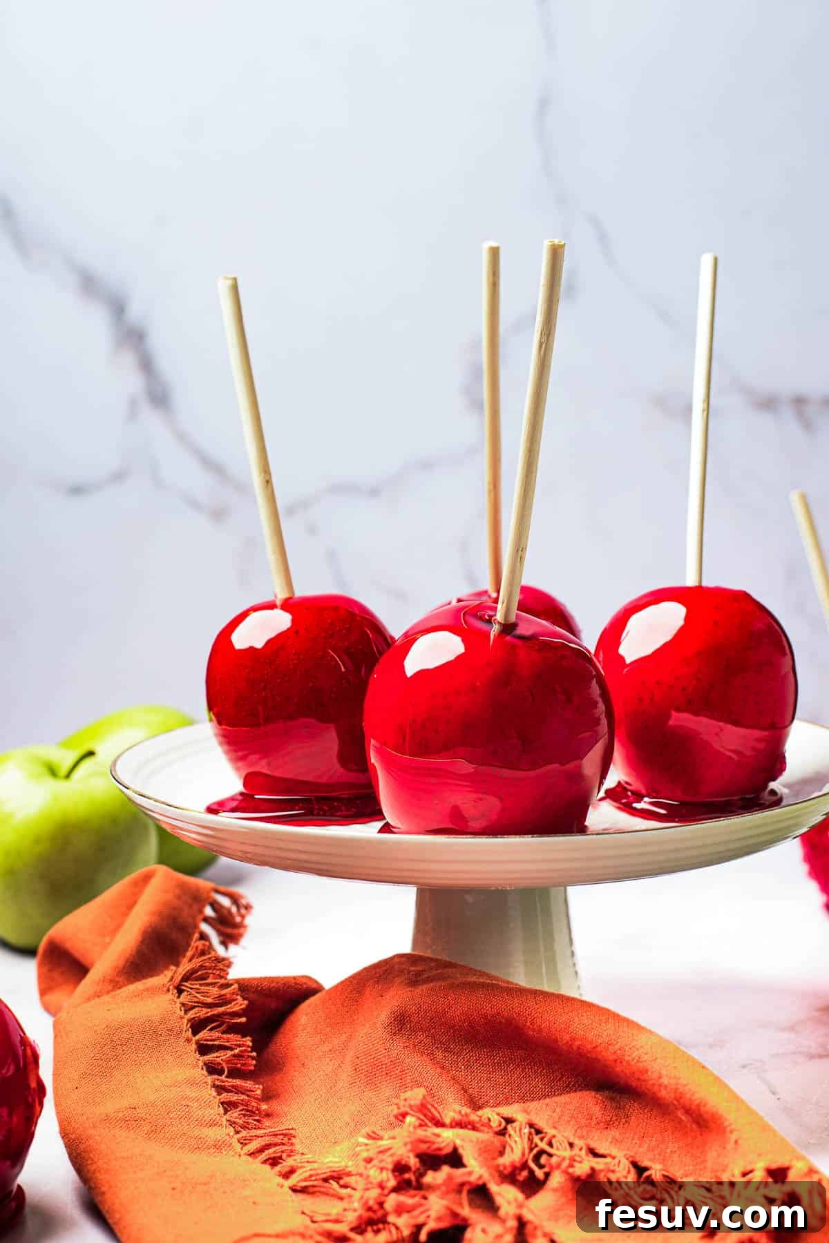A white cake stand elegantly displaying four perfectly candied apples, ready for serving at a festive gathering.
