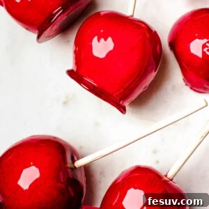 Several candy apples on a white cutting board. Plain Granny Smith apples and an orange fringed placemat in the background.