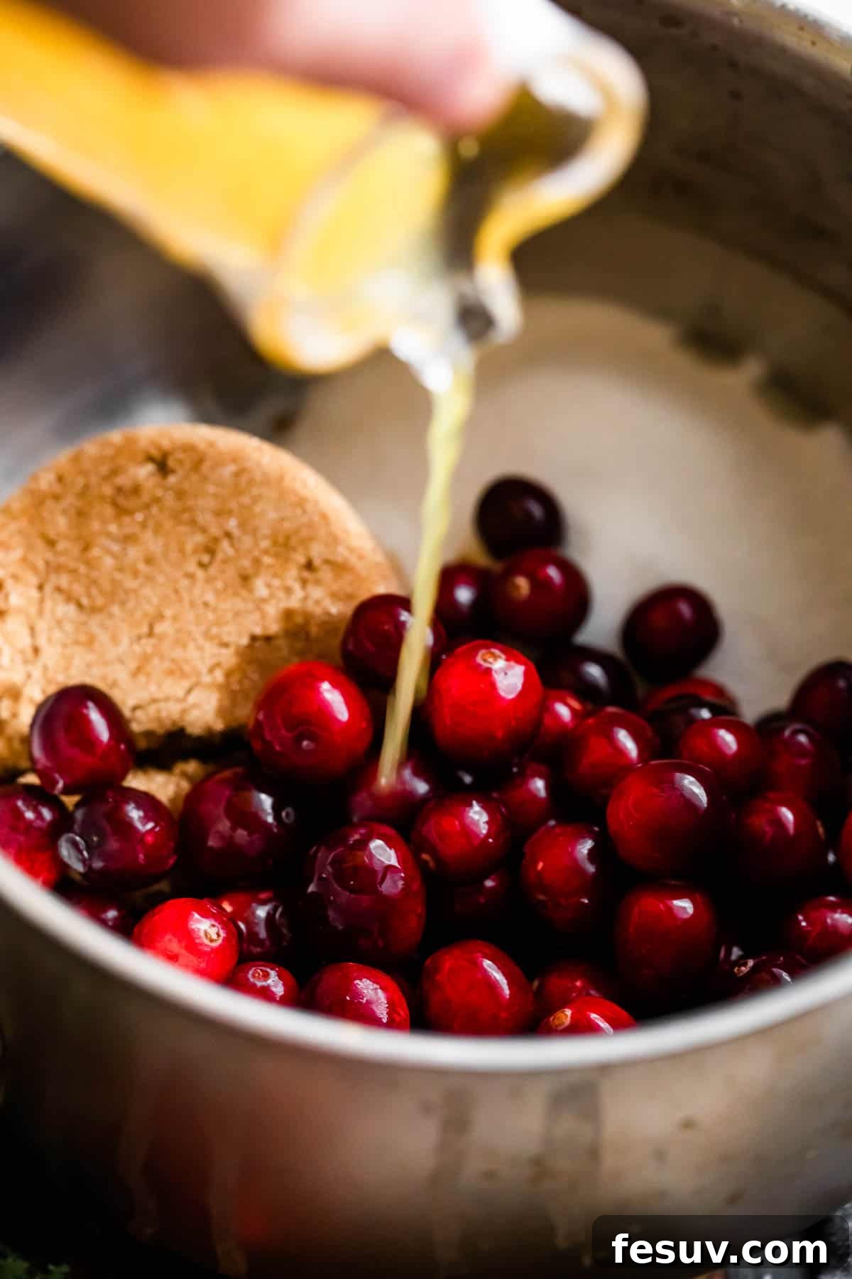 Divine Homemade Cranberry Sauce 4 pouring orange juice over fresh cranberries and sugars inside of a saucepan.