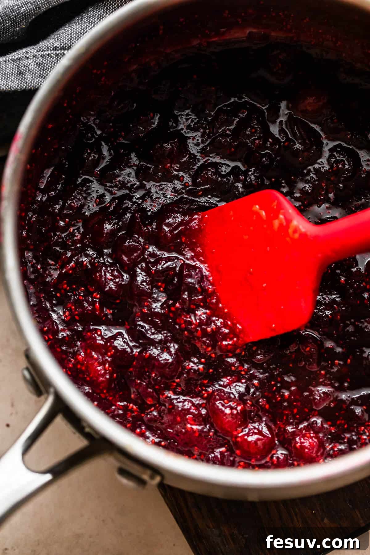 Divine Homemade Cranberry Sauce 5 cooking cranberry sauce in a saucepan and stirring through with a red rubber spatula.